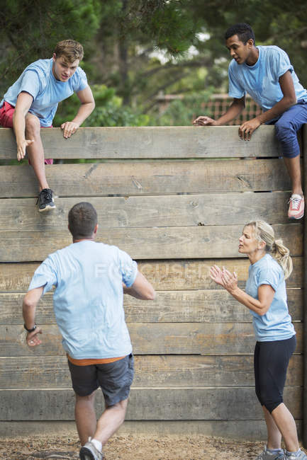Teammates cheering man nearing wall on boot camp obstacle course — Stock Photo