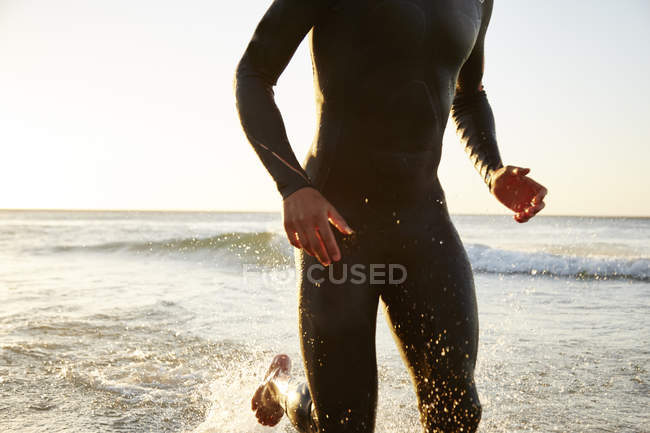 Male triathlete swimmer in wet suit running out of ocean surf — Stock Photo