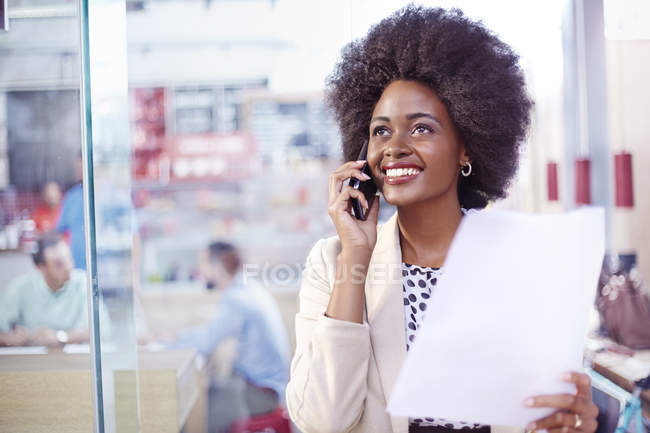 Empresária sorridente com papelada falando por telefone — Fotografia de Stock