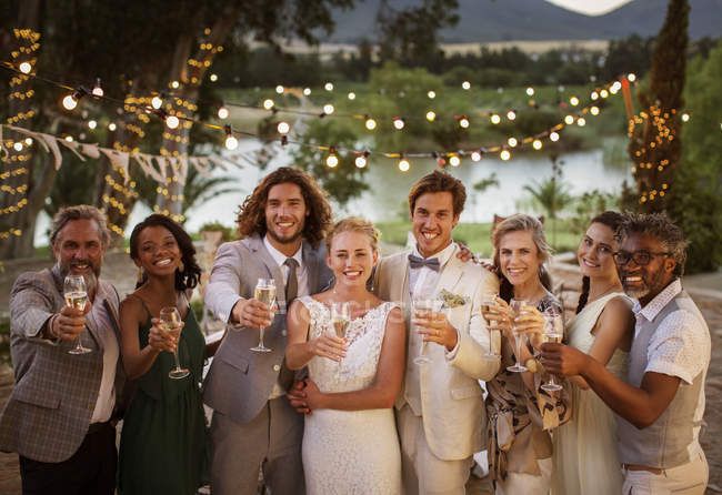 Ritratto di giovane coppia con ospiti brindare con champagne durante il ricevimento di nozze al crepuscolo — Foto stock