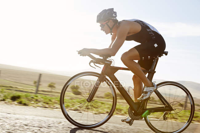 Велогонщик-триатлонист на рассвете на велосипеде по солнечной сельской дороге — стоковое фото