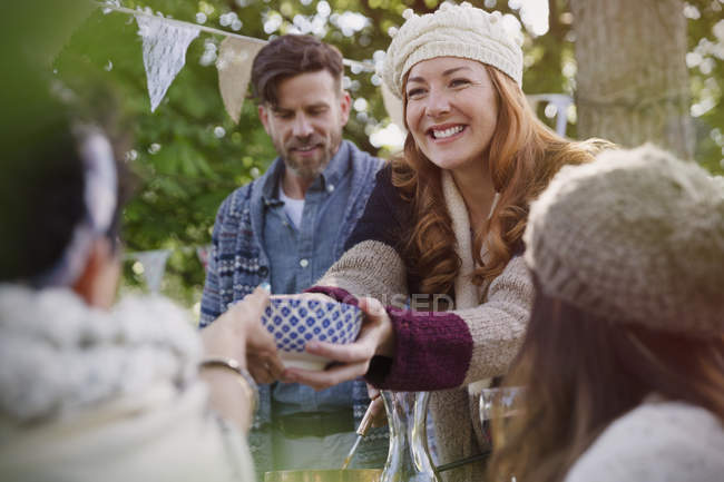 Smiling woman passing food to friend at garden lunch — Stock Photo