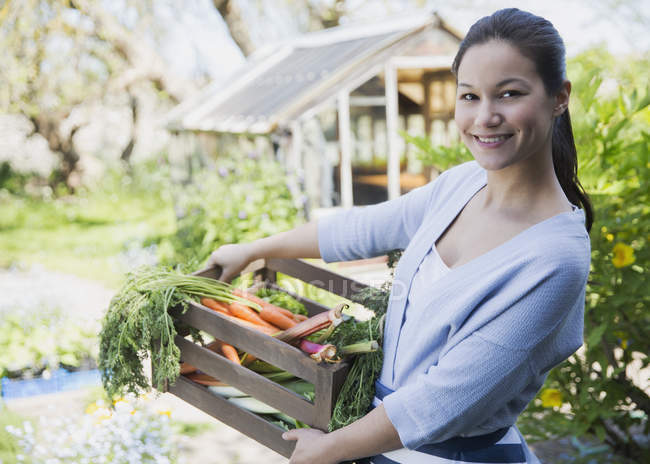 Портрет улыбающейся женщины со свежесобранным ящиком овощей в саду — стоковое фото