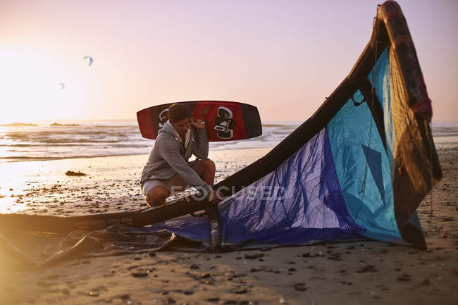 Человек с оборудованием для кайтбординга на пляже на закате — стоковое фото
