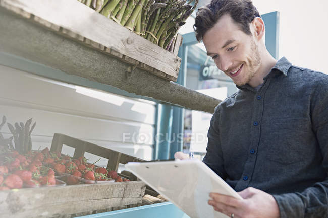 Trabajador de mercado sonriente revisando inventario con portapapeles al lado de fresas - foto de stock