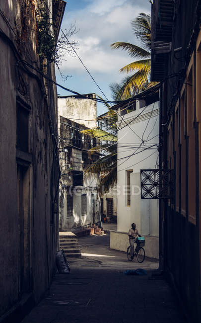 Man riding bicycle on narrow street between buildings, Zanzibar, Tanzania — Stock Photo