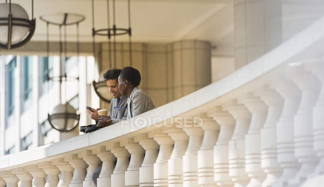 Corporate businessman and businesswoman with coffee and cell phone at railing — Stock Photo