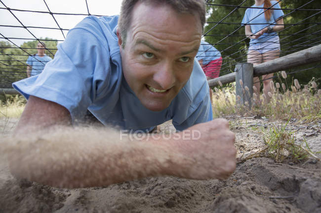 Determined man crawling on boot camp obstacle course — Stock Photo