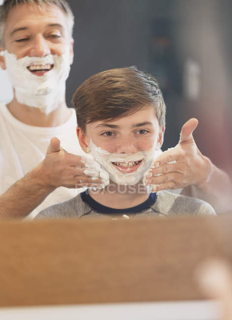 Père aidant fils prétendant se raser dans le miroir de salle de bain — Photo de stock