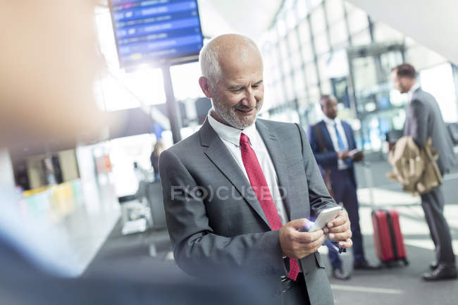 Empresario mensajes de texto con teléfono celular en el vestíbulo del aeropuerto - foto de stock