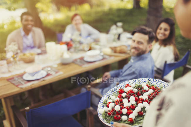 Mujer sirviendo ensalada Caprese aperitivo a amigos en la mesa del patio - foto de stock