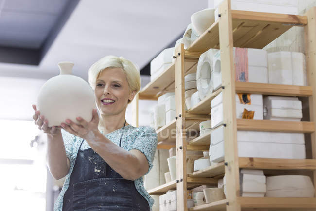 Mujer sonriente sosteniendo jarrón de cerámica en el estudio - foto de stock