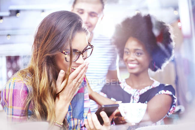 Laughing friends texting with cell phone in cafe — Stock Photo