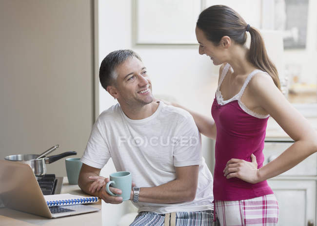 Пара в пижаме разговаривает и пьет кофе за ноутбуком — стоковое фото