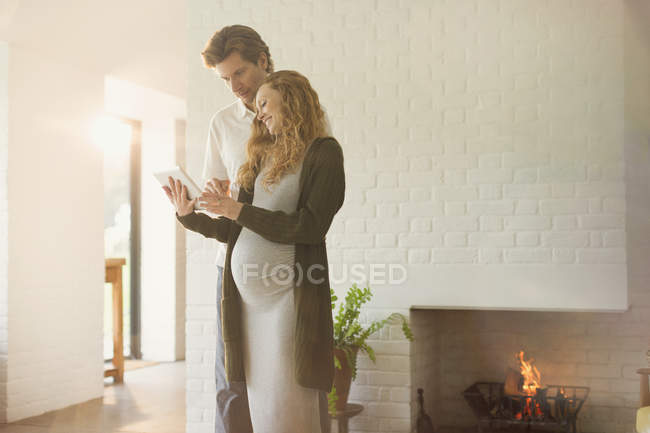 Couple enceinte utilisant tablette numérique près de la cheminée dans le salon — Photo de stock