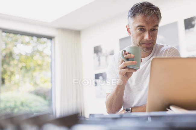Чоловік п'є каву і працює на ноутбуці на кухні — стокове фото