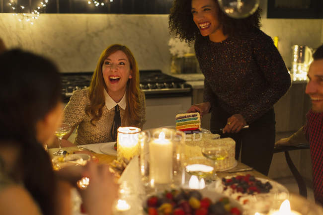 Laughing friends enjoying cake at candlelight Christmas dinner party — Stock Photo