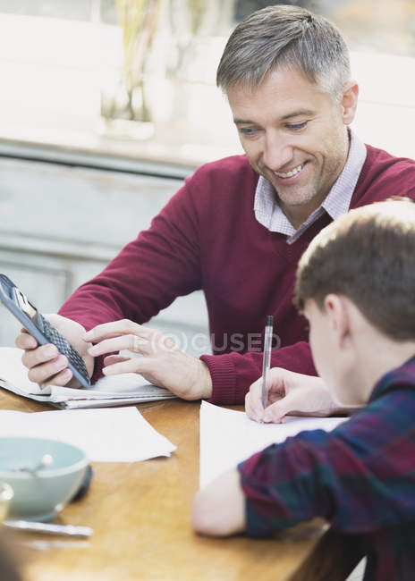 Pai com calculadora ajudando filho fazendo lição de casa de matemática — Fotografia de Stock