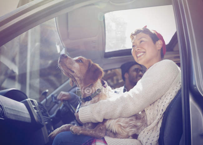 Mujer sonriente sosteniendo perro en la vuelta en el coche - foto de stock