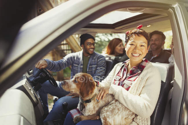 Портрет усміхненої жінки з собакою на колінах в машині з друзями — стокове фото