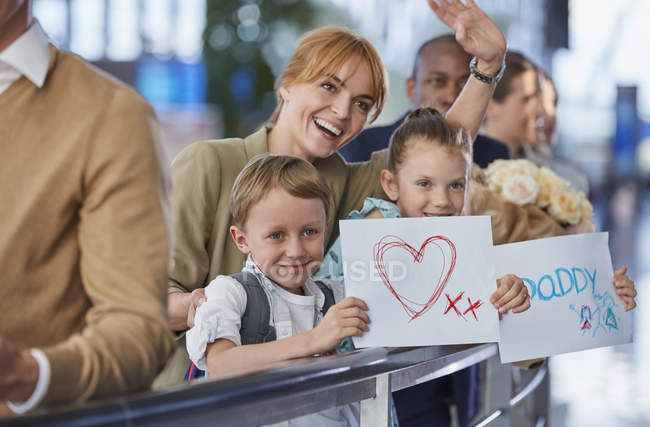 Mãe e filhos com sinais de boas-vindas para o pai no aeroporto — Fotografia de Stock