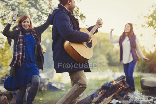 Amici che ballano e suonano la chitarra intorno al falò — Foto stock