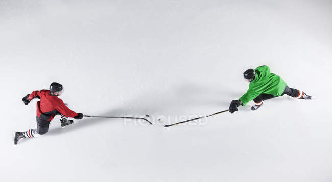 Overhead view hockey opponents reaching for puck on ice — Stock Photo