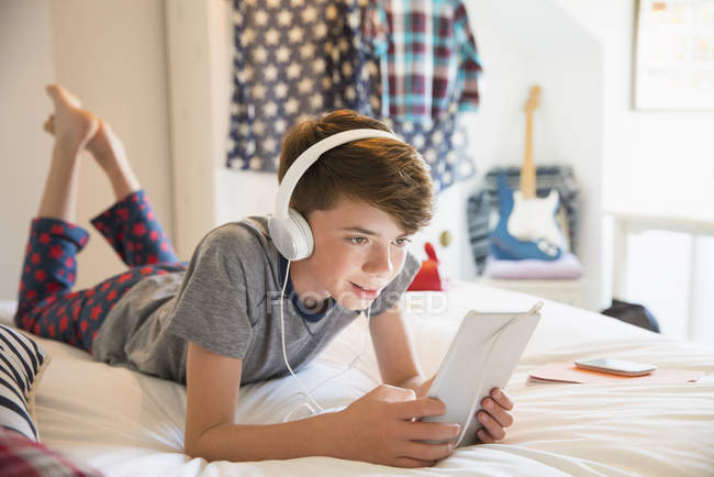 Мальчик с наушниками слушает музыку на цифровом планшете — стоковое фото