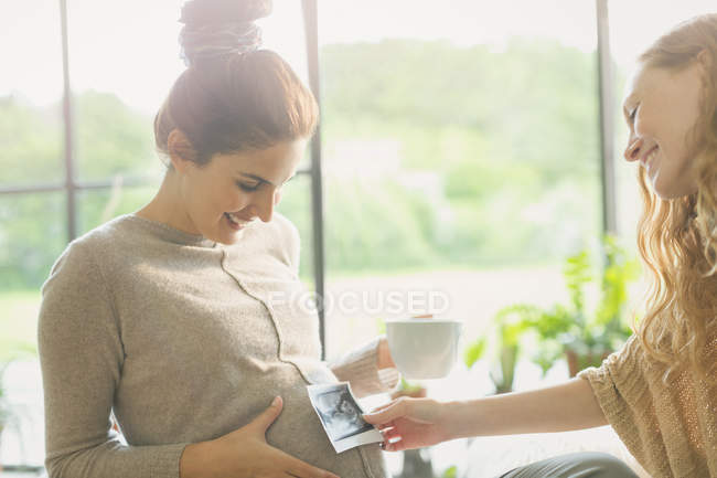 Friend holding ultrasound to pregnant woman?s stomach — Stock Photo