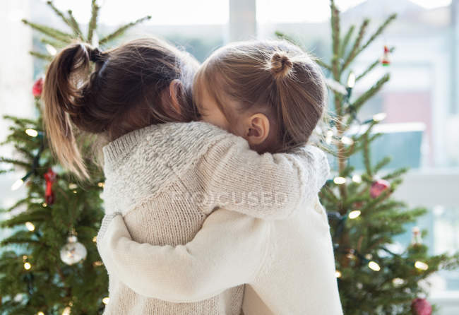 Girls hugging in front of Christmas trees — Stock Photo