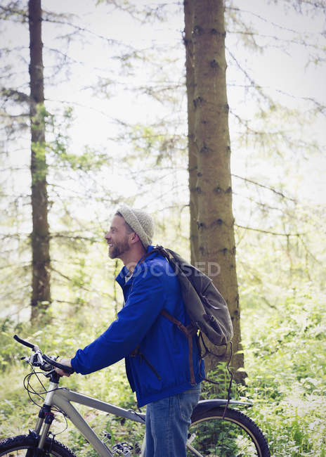 Чоловік з рюкзаком і гірським велосипедом в сонячних лісах — стокове фото