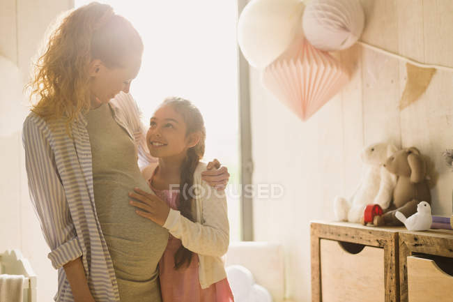 Pregnant mother and daughter in sunny nursery — Stock Photo