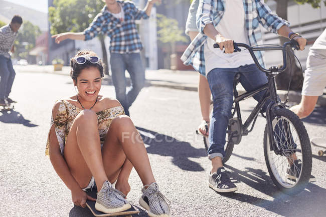 Enthusiastic teenage girl skateboarding with friends on sunny urban street — Stock Photo