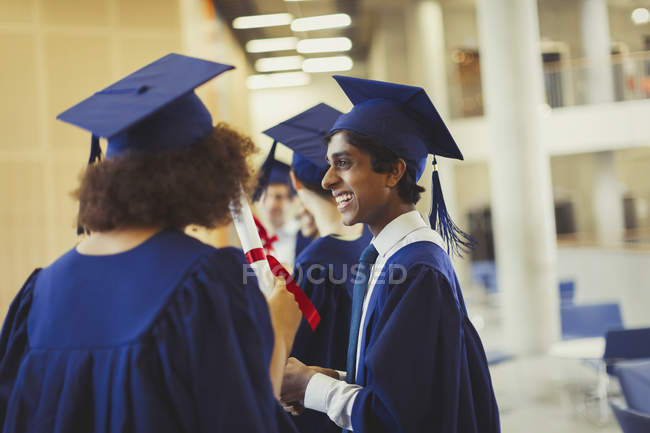 Sorrindo graduados universitários em boné e vestido — Fotografia de Stock