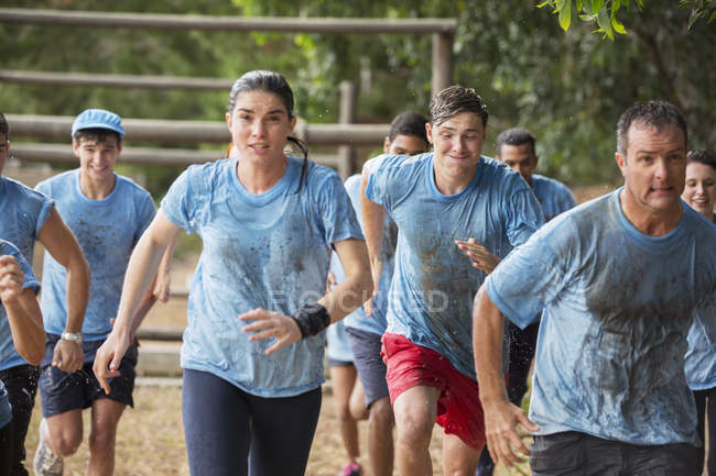 Team running in rain on boot camp obstacle course — Stock Photo