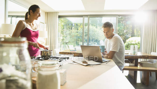 Paar kocht und arbeitet am Laptop in der Morgenküche — Stockfoto