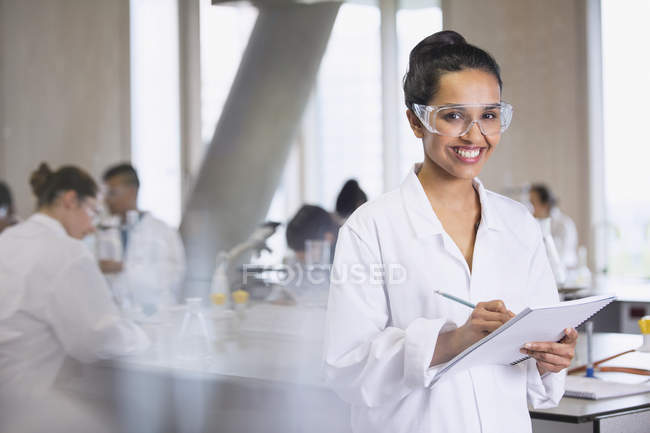 Portrait d'une étudiante souriante prenant des notes dans une salle de classe de laboratoire de sciences — Photo de stock