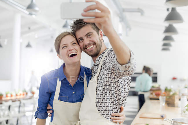 Enthusiastic couple taking selfie with camera phone in cooking class kitchen — Stock Photo