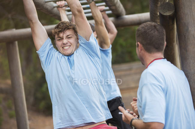 Determined man crossing monkey bars on boot camp obstacle course — Stock Photo
