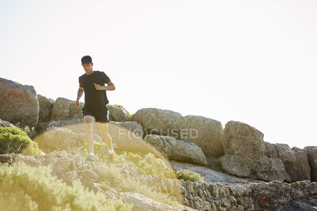 Hombre triatleta corriendo en sendero rocoso soleado - foto de stock