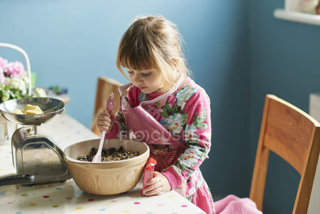 Curious girl baking with mixing bowl in kitchen — Stock Photo