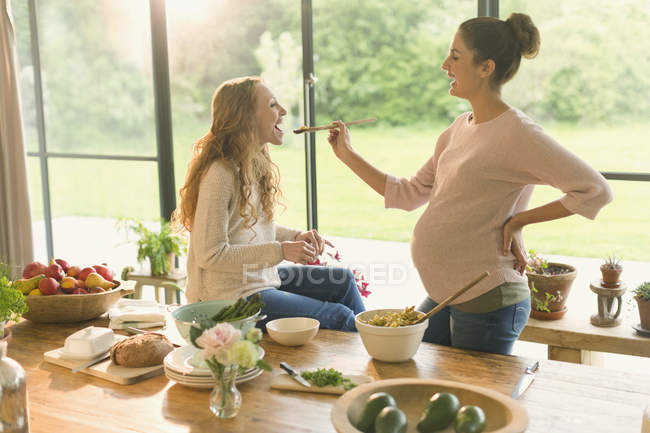 Mujeres embarazadas cocinando y degustando alimentos en la mesa - foto de stock