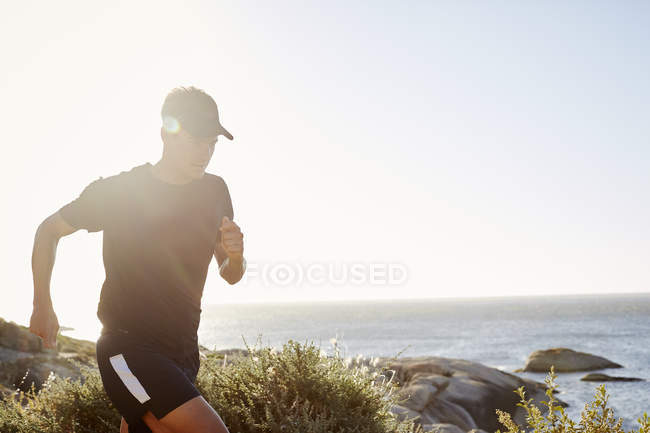 Corredor de triatleta masculino corriendo a lo largo del océano - foto de stock