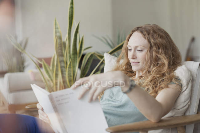 Frau liest Buch im Sessel — Stockfoto