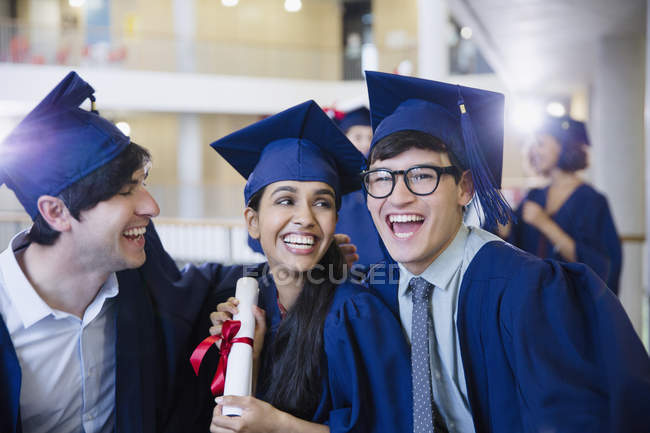 Felices graduados universitarios en gorra y vestido celebrando con diploma - foto de stock