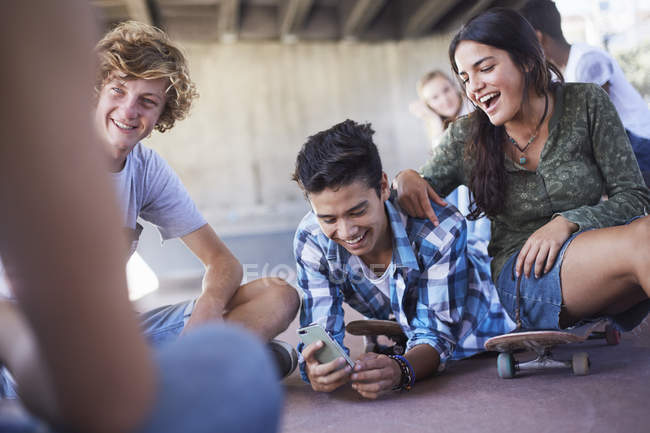 Amigos adolescentes colgando mensajes de texto con el teléfono celular en el parque de skate - foto de stock