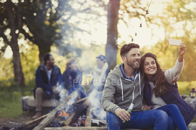 Sorrindo casal tomando selfie com telefone da câmera perto da fogueira — Fotografia de Stock
