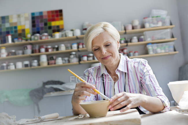 Smiling mature woman painting pottery bowl in studio — Stock Photo