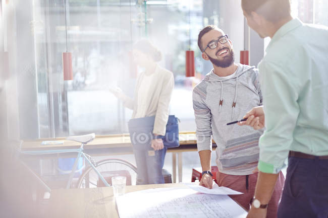 Smiling architects talking and reviewing blueprints — Stock Photo