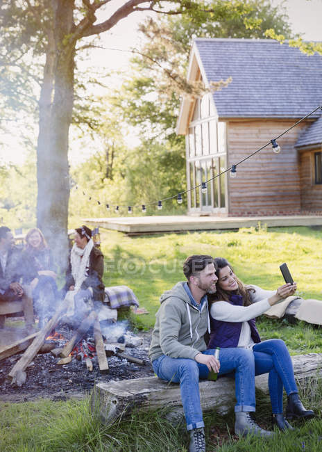 Пара, делающая селфи с телефоном у костра возле домика — стоковое фото